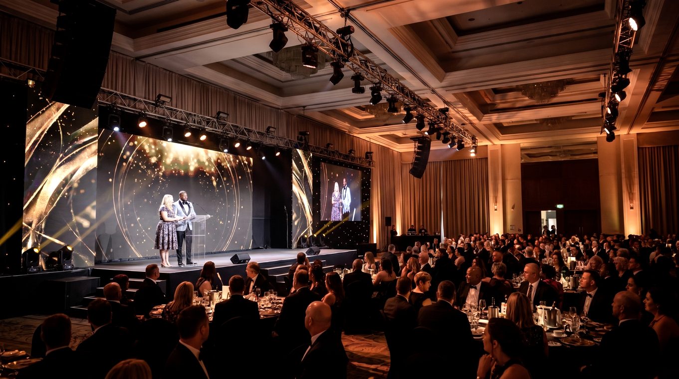 A full ballroom in black tie, the stage lit